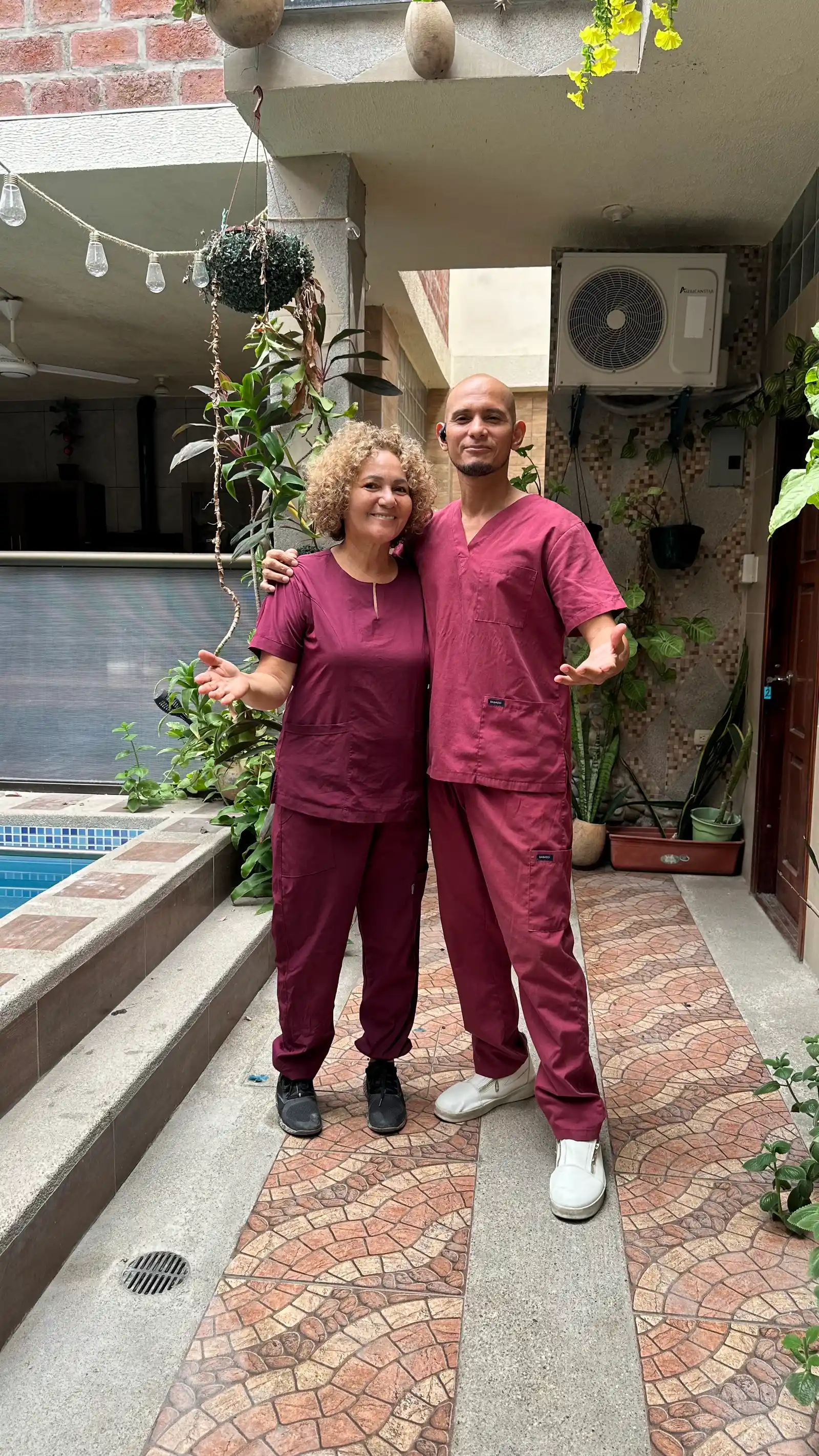 Dos integrantes de SIRONA posan con uniforme color vino en un pasillo con plantas, junto a la piscina.