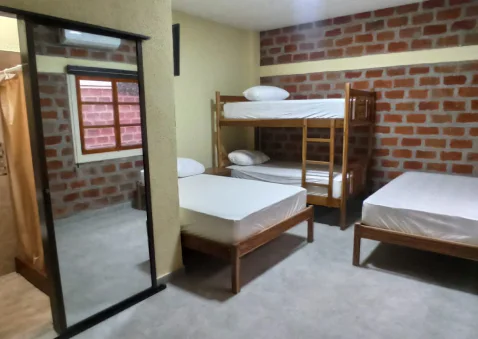 Habitación con camas de madera, una litera y paredes de ladrillo visto.