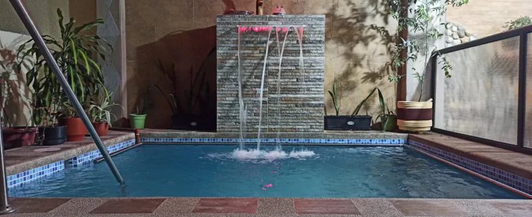 Piscina interior con una cascada de agua y plantas alrededor.