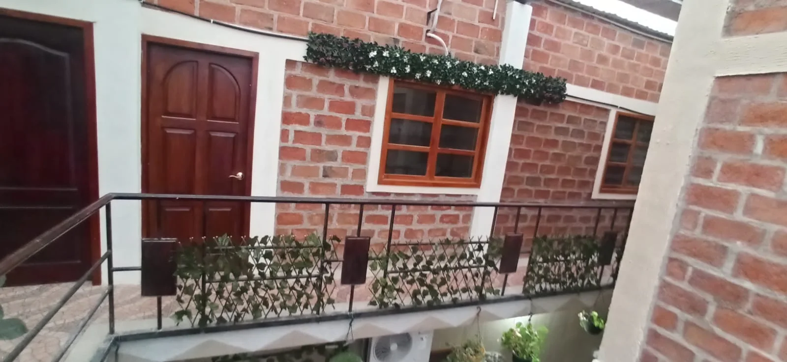Pasillo interior de la casa de huéspedes, con puertas de madera, ladrillo y plantas.